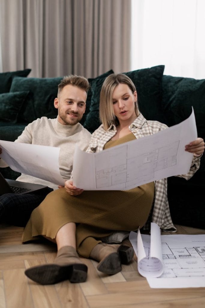 A couple sitting on the floor, examining house blueprints in a cosy home setting.